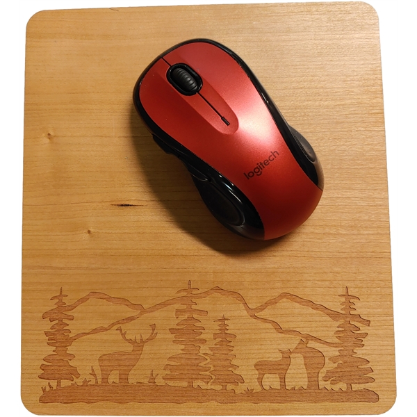 A laser-engraved wood mousepad with a red logitech wireless mouse on it. The laser engraving shows mountains, trees, and deer. Sustainable creative accessories.